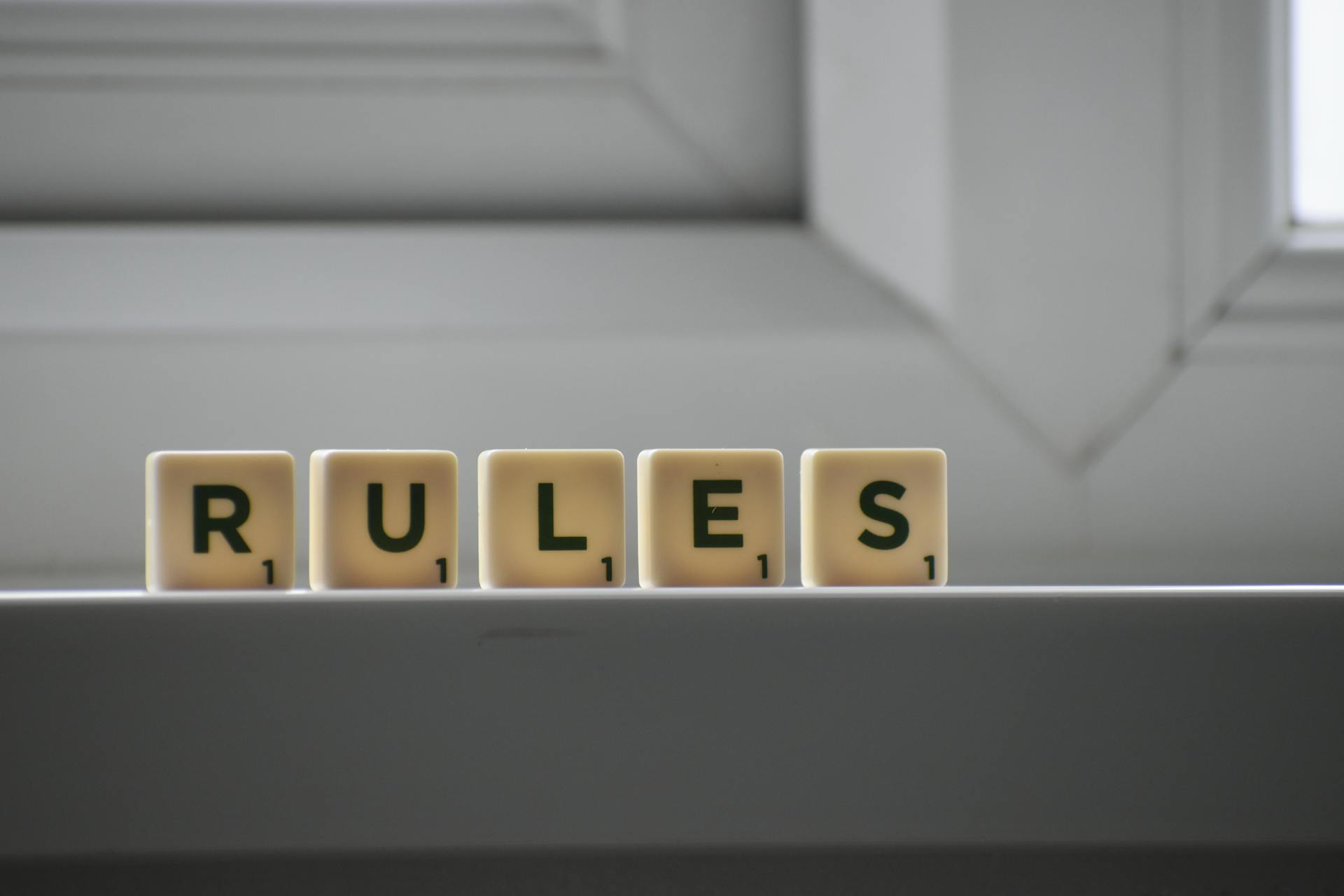 Identical small square shaped cubes with RULES title and numbers on white windowsill near window in house in daylight