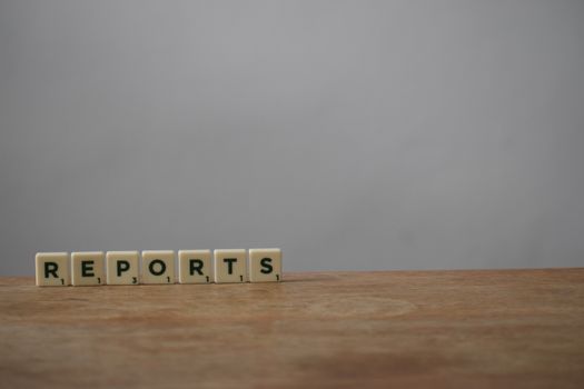 Scrabble tiles spelling 'reports' on a wooden desk, ideal for office or business themes.
