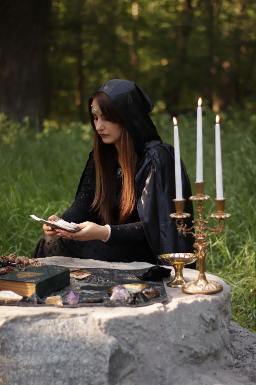 Free A woman dressed in black performs a mystical ritual in a forest setting with candles and stones. Stock Photo