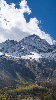 Stunning view of snow-capped Siguniang Mountain against a bright blue sky and scattered clouds.