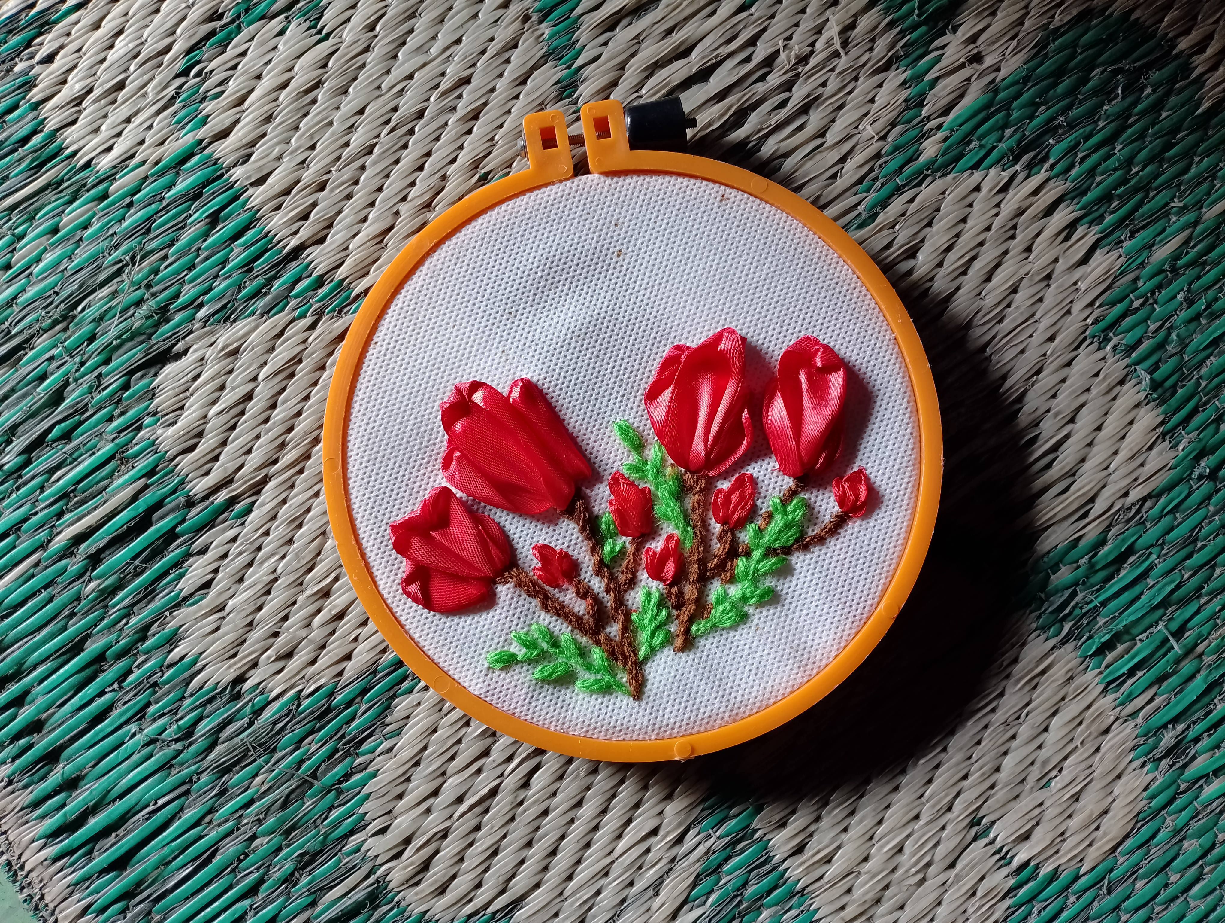 Colorful floral embroidery displayed in a hoop frame on woven mat background.