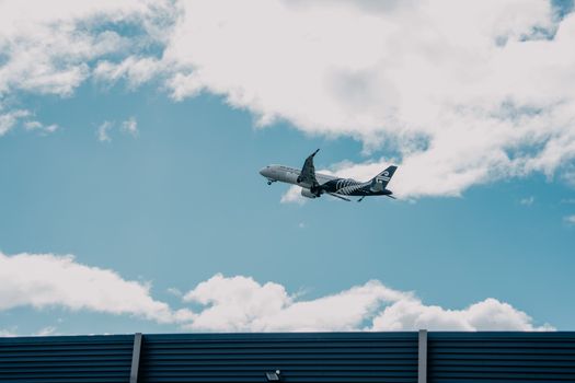 Airplane soaring above a building with cloudy skies in New Zealand.