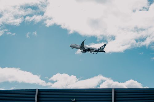 Free Airplane soaring above a building with cloudy skies in New Zealand. Stock Photo