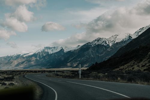 Free Curving road leading through breathtaking New Zealand mountains under a cloudy sky, showcasing natural beauty. Stock Photo