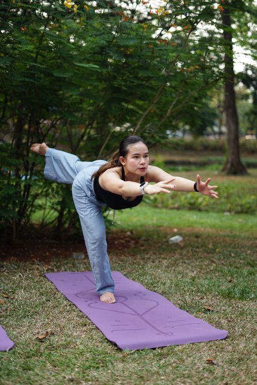 Free Young woman balances in yoga pose on mat outdoors, surrounded by greenery. Stock Photo