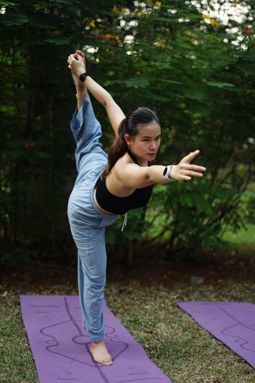 Free Young woman performing a yoga pose on a mat in a lush outdoor setting. Stock Photo