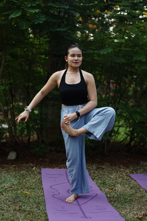 Free A woman practices yoga outdoors on a purple mat surrounded by greenery, demonstrating balance and focus. Stock Photo