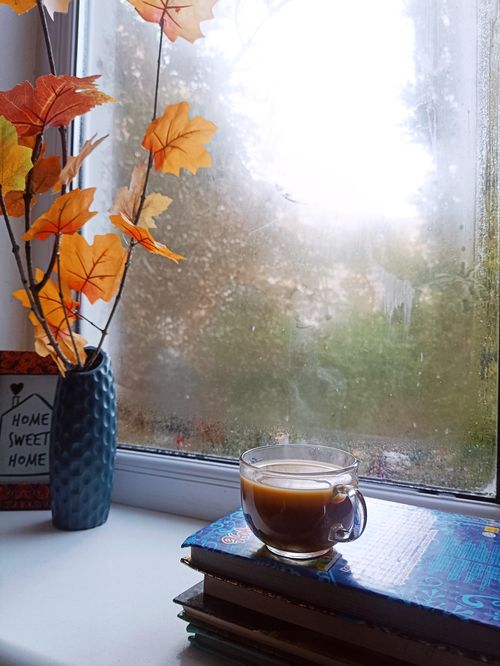 Free A cozy shot of a coffee cup by a window with autumn leaves indoors. Stock Photo