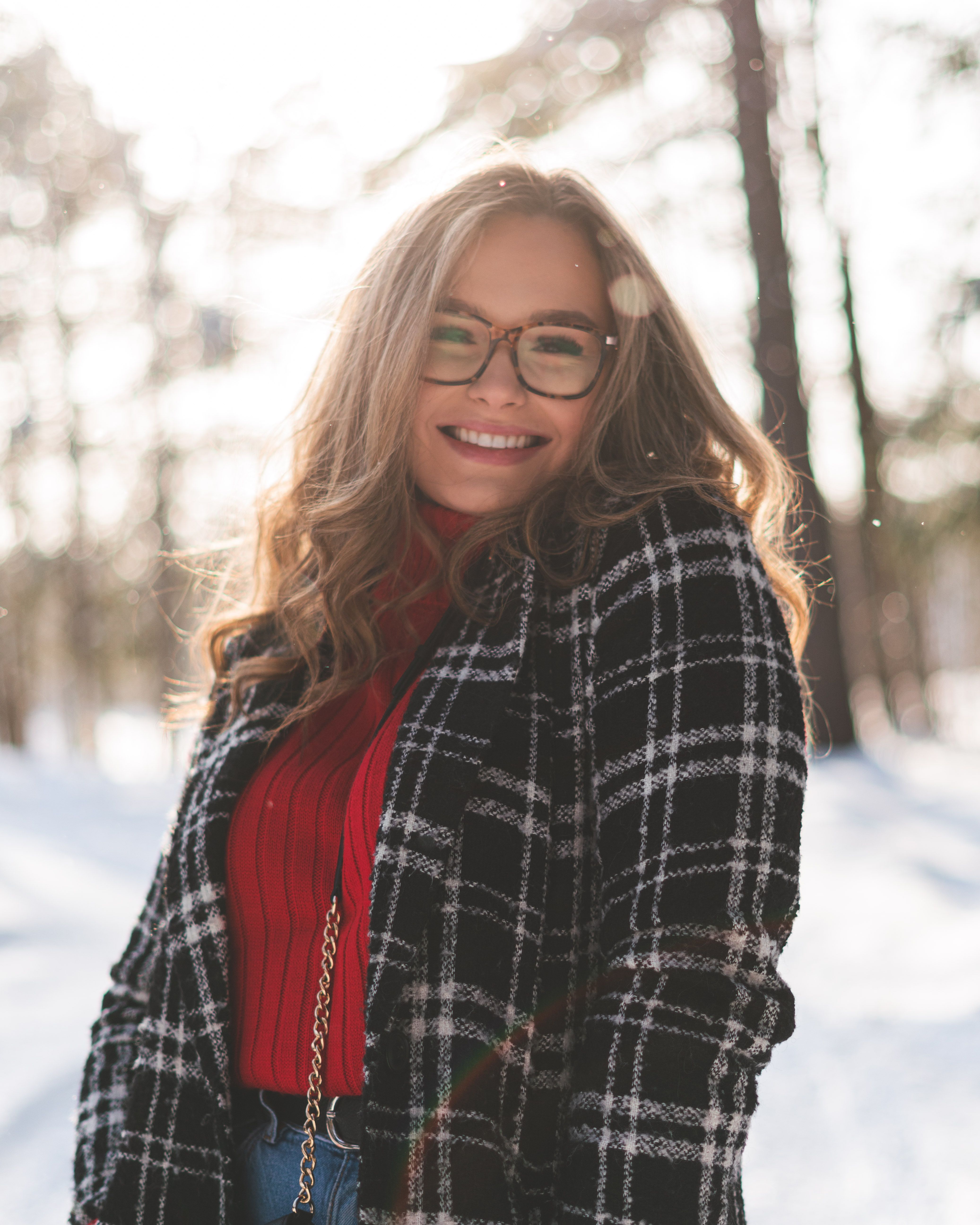 Smiling woman in winter attire surrounded by snow-covered trees, enjoying a sunny day.