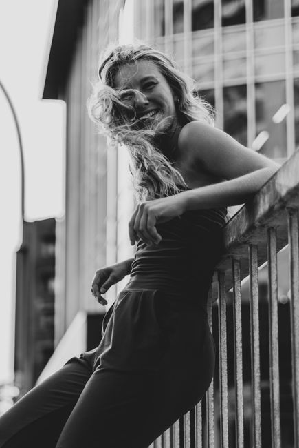 Captivating black and white portrait of a smiling woman leaning on a railing outdoors.
