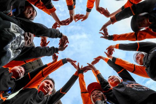 Free Dynamic image of a youth group making a circle with raised hands against a blue sky. Stock Photo