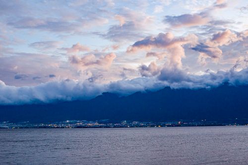 Free Vibrant clouds and city lights over mountains at twilight create a dramatic scene. Stock Photo