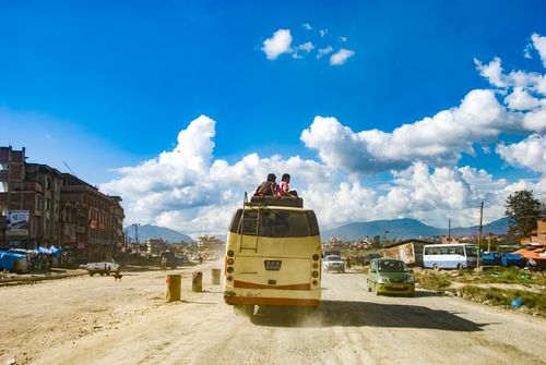 Free Bus carrying passengers on roof through rural Kathmandu, Nepal, under vibrant blue skies. Stock Photo