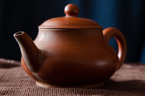 Free An elegant brown ceramic teapot displayed on a textured fabric, showcasing its classic design and warm tones. Stock Photo