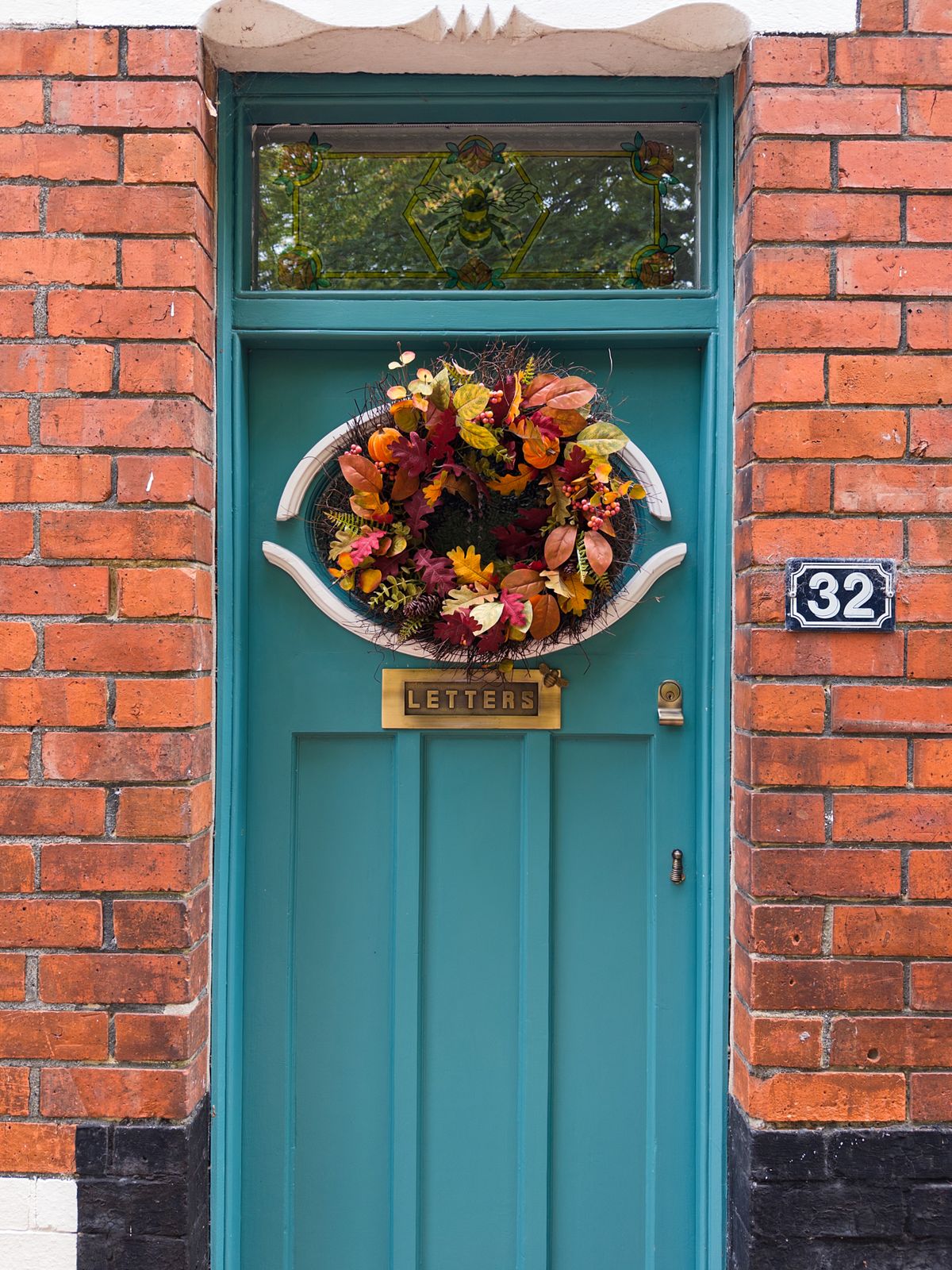 Teal front door with an autumn wreath against red brick