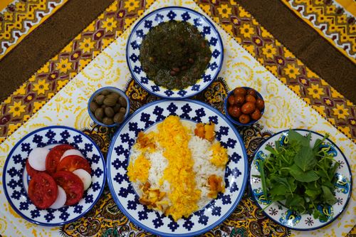 Free Vibrant Persian dishes with saffron rice, herbs, olives, and more on a decorative rug. Stock Photo