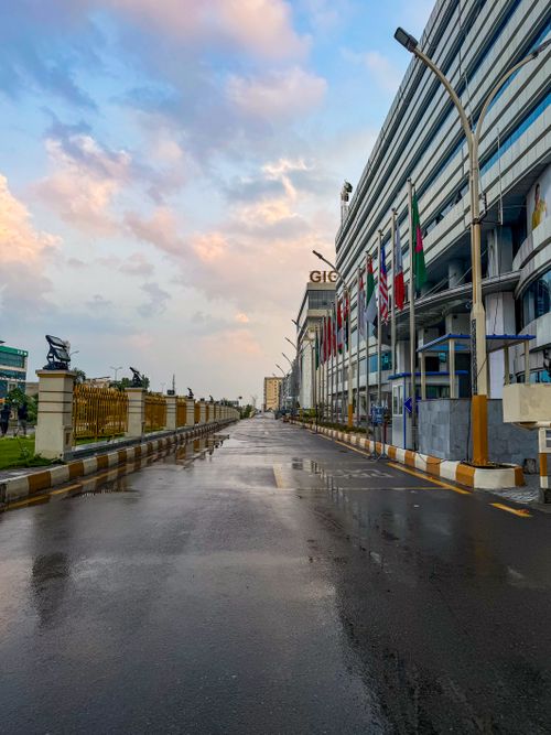 Free An empty street reflecting the sky, surrounded by modern architecture and international flags. Stock Photo
