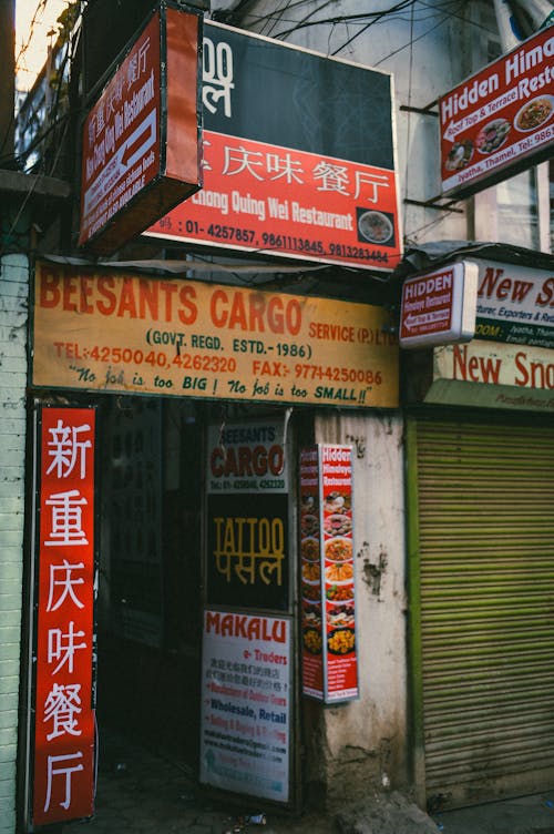 Bright signboards with MAKALU title and hieroglyphs with symbols and numbers on aged house with rough shabby walls and ribbed fence in Asian town in daylight