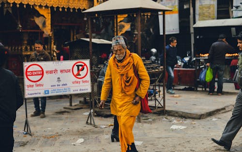 Senior Hindu man in bright cloths walking on dirty street