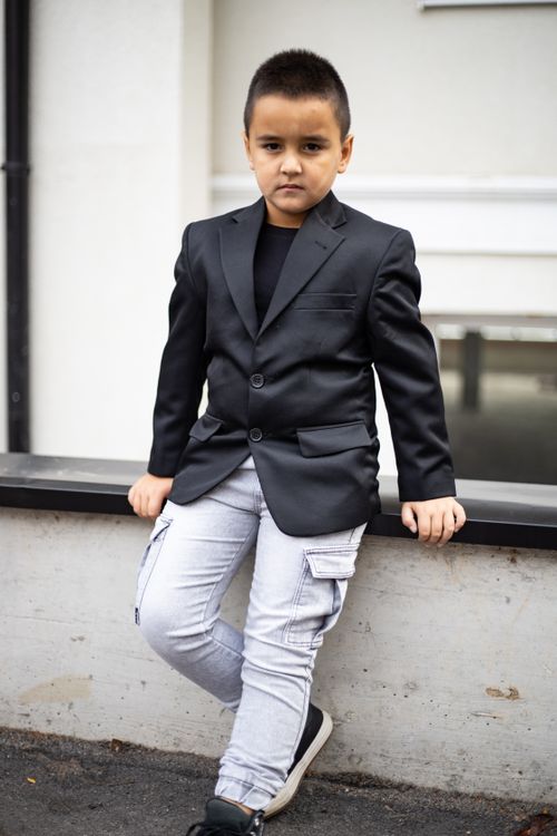Free Young boy dressed in a black blazer and jeans confidently posing outdoors for a portrait. Stock Photo