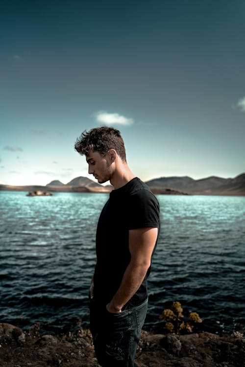 Free Man In Black Crew Neck T-shirt Standing Near Body Of Water Stock Photo