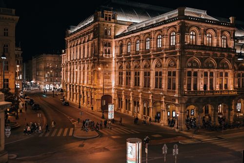 Free Stunning night view of Vienna State Opera building illuminated with warm lights and street activity. Stock Photo