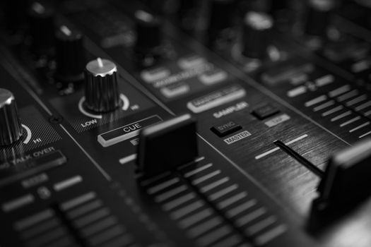 High-contrast close-up of an audio mixer with sliders and knobs in a black and white tone.