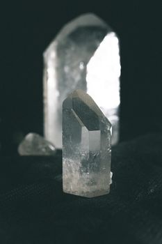 Big rough gem with shiny surface glowing near small transparent vertical gemstone on table in flat at night on black background
