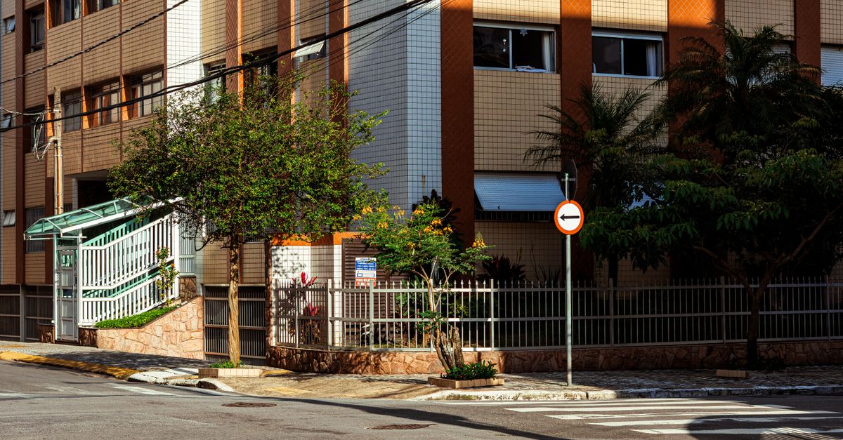 Street view of a modern apartment building with sunlight and greenery.