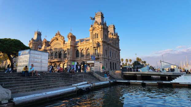 A stunning sunset view of the historical Port Authority building in Barcelona, Spain, with people enjoying the surroundings.