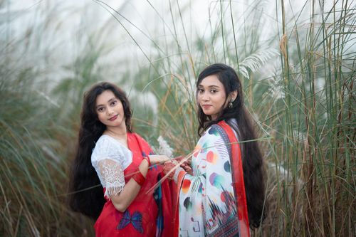 Free Two women in traditional attire amidst serene Kash flowers in Bangladesh Stock Photo
