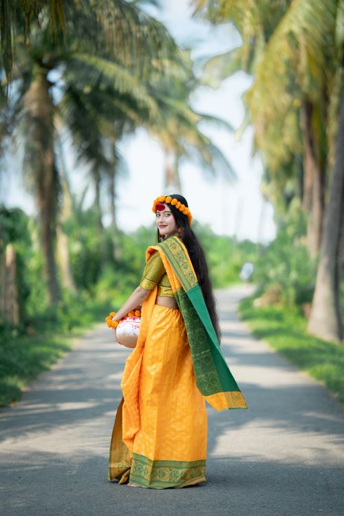 Free A beautiful South Asian woman wearing a traditional yellow and green saree, captured on a lush outdoor path. Stock Photo