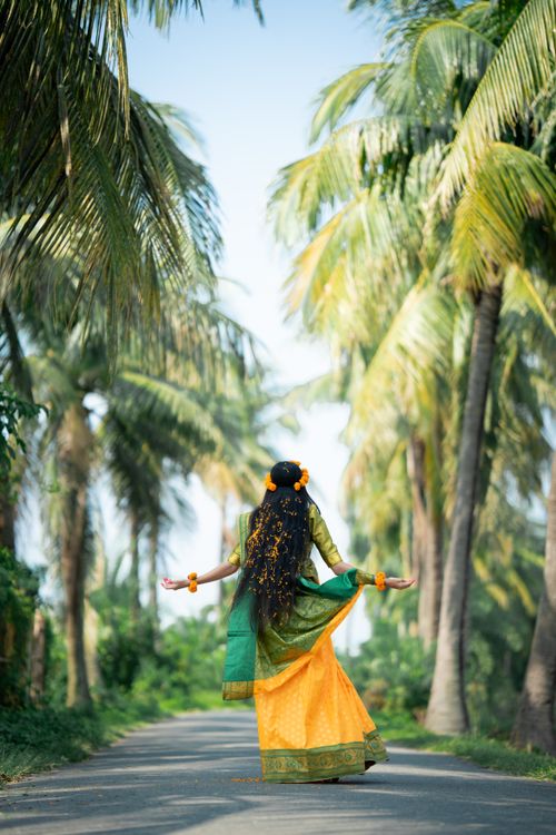 Free South Asian woman in vibrant saree dancing amidst lush palm trees outdoors. Stock Photo