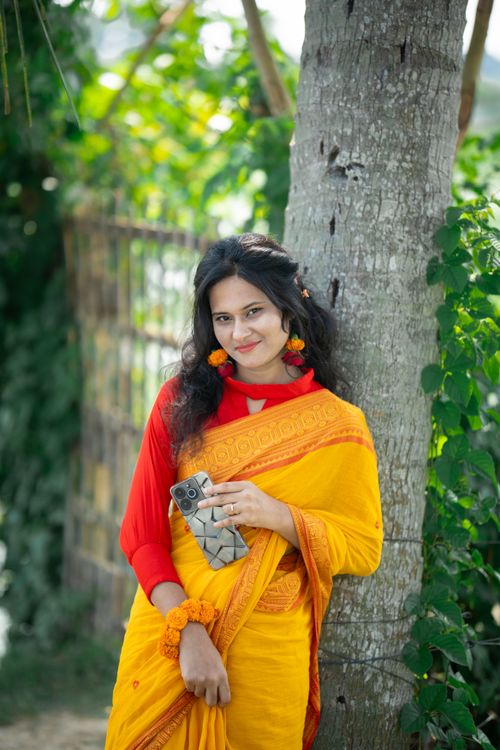 Free South Asian woman in a vibrant yellow saree, embodying traditional Bangladeshi fashion against a lush outdoor backdrop. Stock Photo