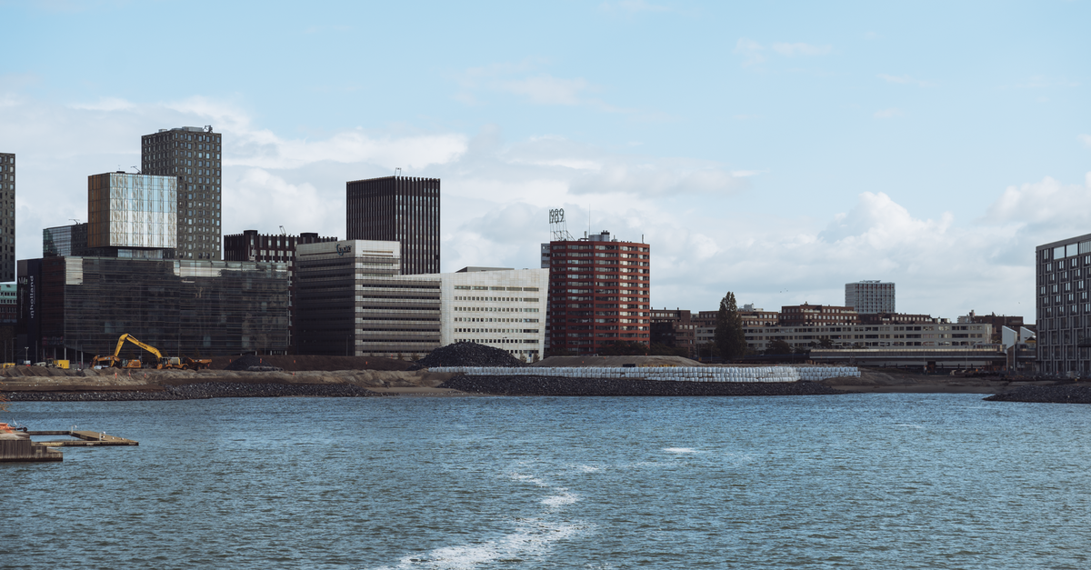 Contemporary cityscape of Rotterdam featuring skyscrapers by the river under a clear sky.