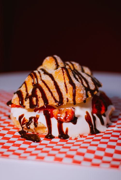 Free Close-up of a dessert with cream filling, strawberries, and chocolate drizzle on a checkered paper. Stock Photo