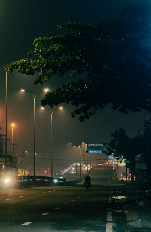 Free A misty urban street at night with dim street lights and a distant bridge. Stock Photo