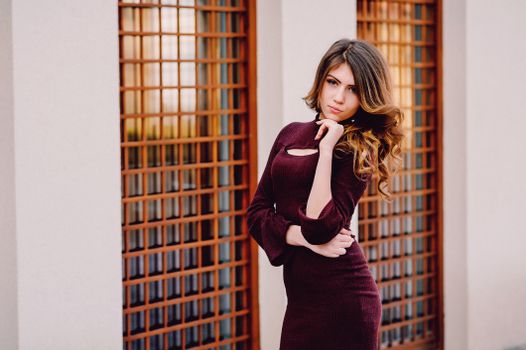 A fashionable woman poses outdoors in a stylish maroon dress, showcasing modern elegance.