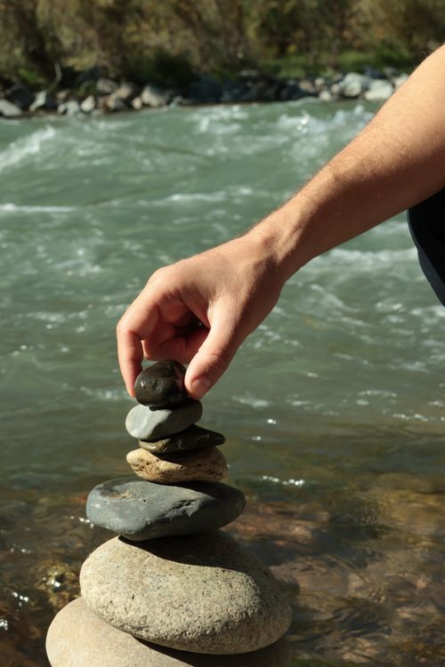 Free A person stacking stones by a river, symbolizing balance and tranquility. Stock Photo