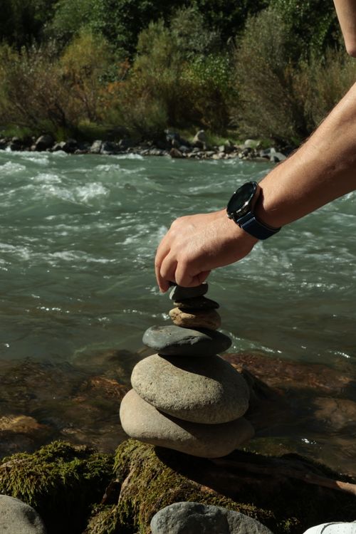 Free A person stacking stones by a tranquil river, symbolizing balance and nature. Stock Photo