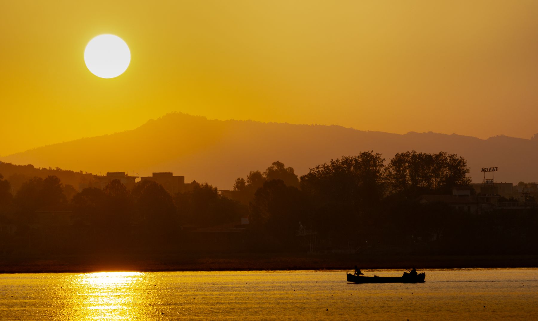 A picturesque sunset over Rawal Lake, Islamabad, with silhouetted boaters and distant hills.