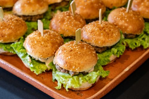 Free Appetizing mini burgers topped with sesame seeds and fresh lettuce served on a platter, perfect for events. Stock Photo