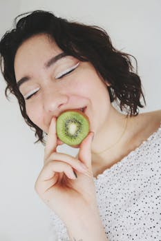 Smiling woman holding and enjoying a fresh slice of kiwi fruit, close up.