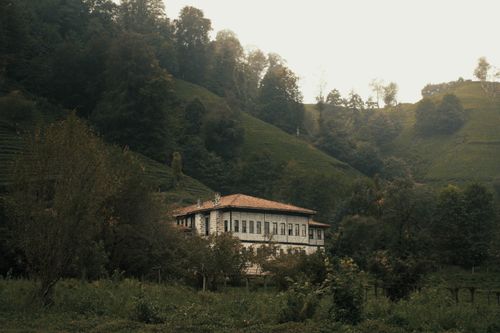 Free Serene countryside view with a rustic house surrounded by lush greenery and hills. Stock Photo