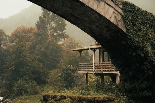 Free Scenic view of a rustic hut beneath an arch bridge in a lush autumn forest. Stock Photo