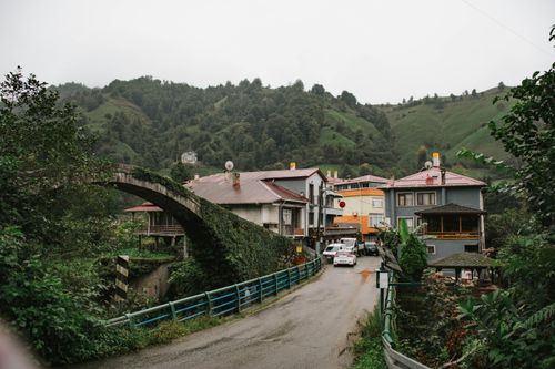 Free Picturesque view of a quaint village with lush green hills and a stone bridge. Stock Photo