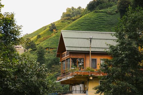 Free Scenic view of a wooden house nestled in vibrant green hills, offering a serene escape into nature. Stock Photo