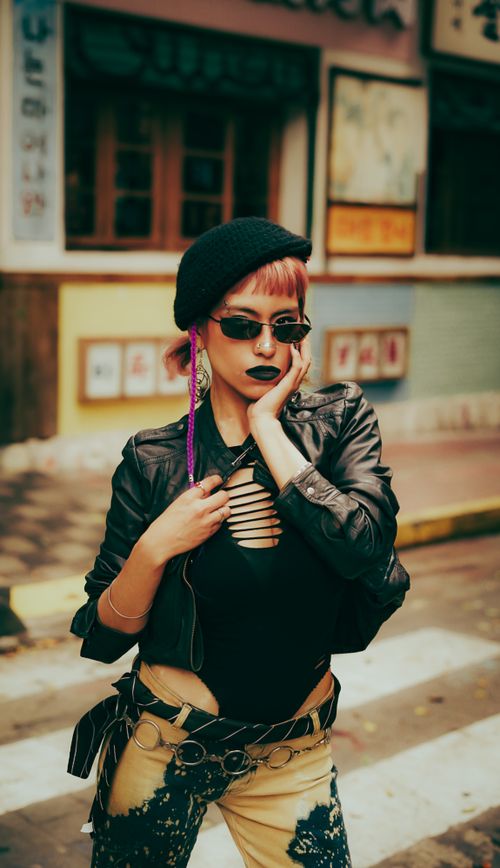 Free Fashionable woman in edgy attire and sunglasses posing confidently on city street. Stock Photo