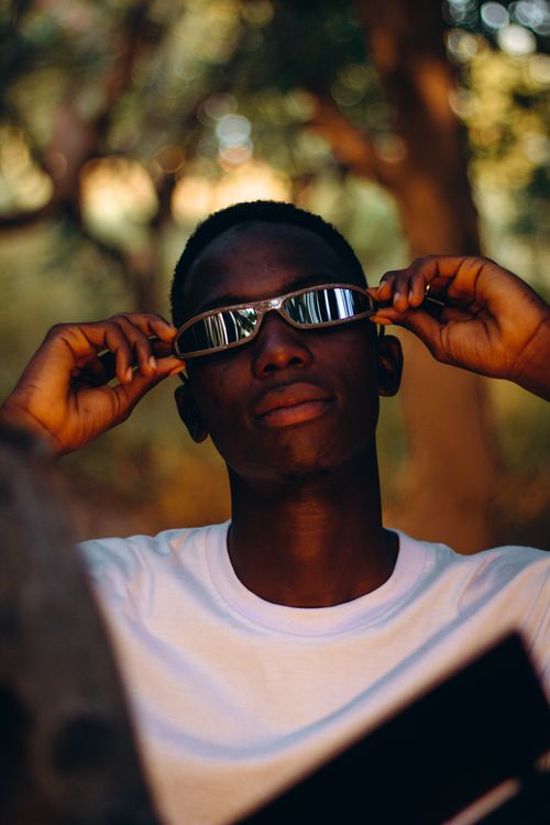 Free Young man in sunglasses adjusting frames, relaxed pose, natural outdoor setting. Stock Photo