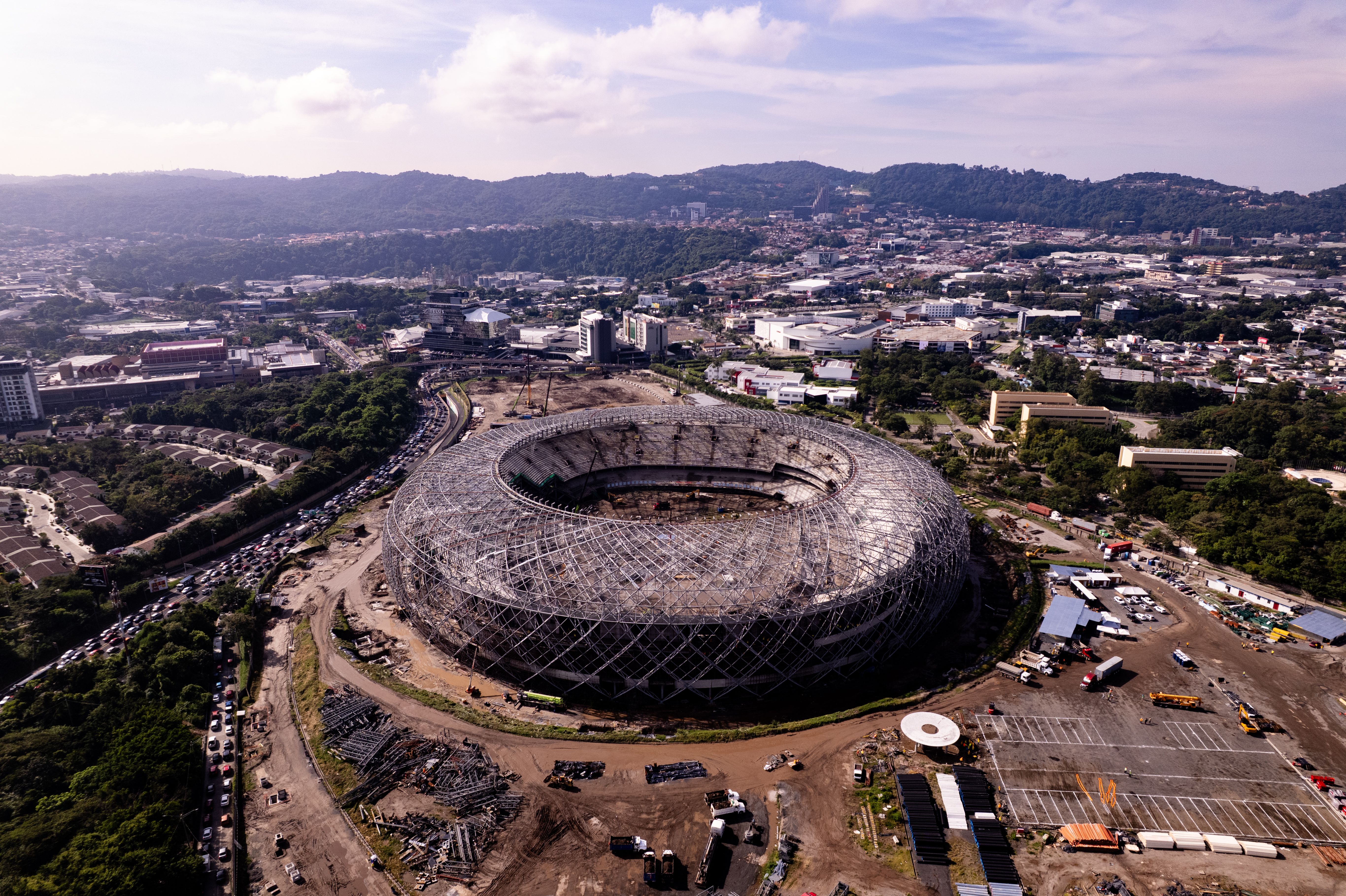 Aerial shot of stadium construction site in San Salvador, showcasing city skyline and surrounding landscapes.